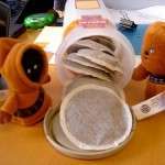 Plush toys exploring tea bags on desk.