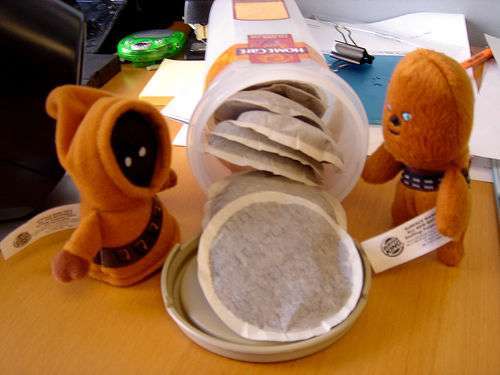 Plush toys exploring tea bags on desk.